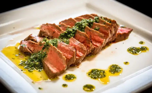 Viipaloitua flank steakia chimichurri-kastikkeella valkoisella lautasella.