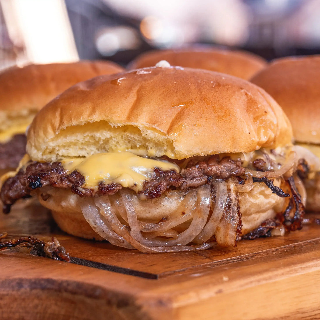 Oklahoma onion burger jauhelihapihvillä, cheddarjuustolla, karamellisoiduilla sipuleilla ja perunasämpylällä, tarjoiltuna puulaudalla.