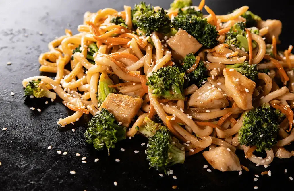 Stir fry kanaa ja nuudeleita Blackstone ParilaGrillillä, sisältäen broilerin lihaa, Chow Mein -nuudeleita, parsakaalia ja seesaminsiemeniä