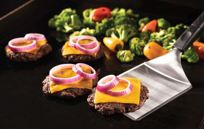Blackstone hampurilaispakkaus käytössä, hampurilaiset juustolla ja punasipulilla paistumassa grillipannulla, vierellä kasvikset
