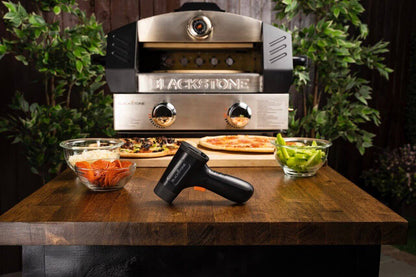 Blackstone Infrapuna Laserlämpömittari keittiön työtasolla pizza-aineksien ja pizzauunin edessä, taustalla viheriöä kasvillisuutta.