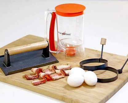 Blackstone Pro Aamupalapakkaus setti, jossa taikina-annostelija, kananmunat, pekoni ja paistovälineet leikkuulaudalla
